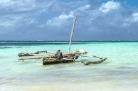 A person fishing from a small boat in clear turquoise waters under a blue sky.