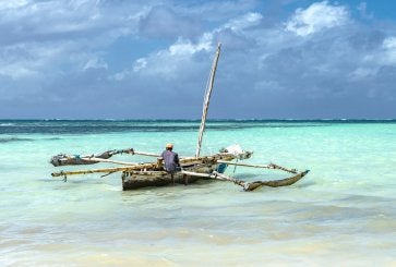 A person fishing from a small boat in clear turquoise waters under a blue sky.
