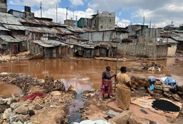 Two people stand on a muddy area near waterlogged homes in Mathare, an informal settlement in Nairobi..