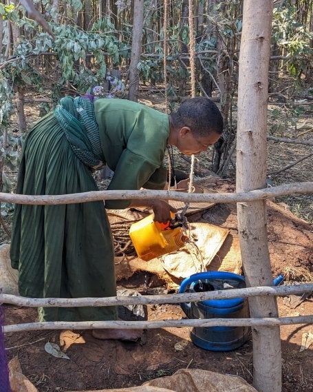 A woman fills a jug with water from an outdoor well.