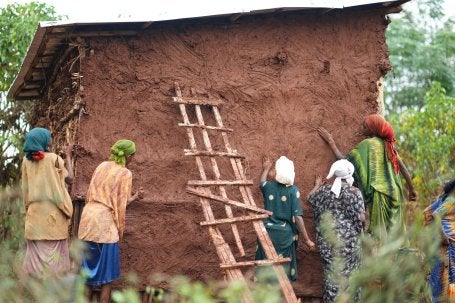 Women repairing the side of a small home.