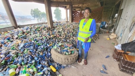 A participant of a recycling network program in Bukavu, DRC, stands next to a large pile of collected waste plastic