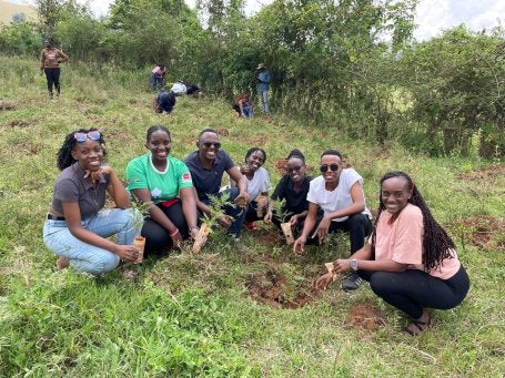 Group of people planting trees in a grassy field, smiling and posing together.