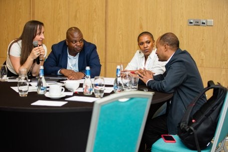 A group of four people engaged in a discussion around a table with water bottles and documents.
