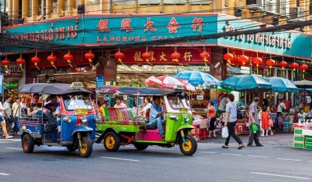 Passengers on a busy Bangkok street ride on colorful three-wheeled tuk-tuks.