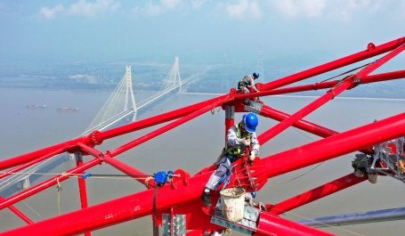 Workers on a power transmission tower overlooking a river.