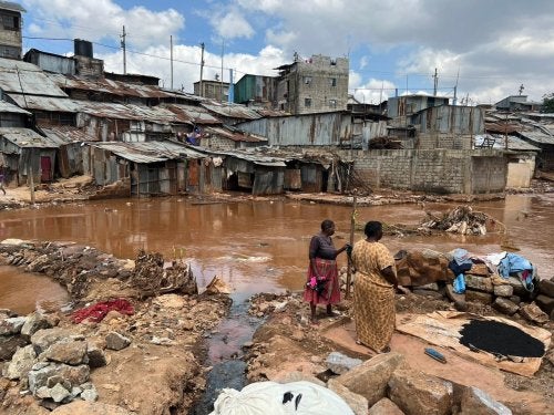 Two people stand on a muddy area near waterlogged homes in Mathare, an informal settlement in Nairobi..